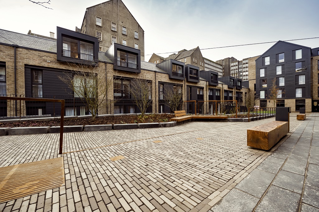A modern city apartment building with square windows and a paved courtyard