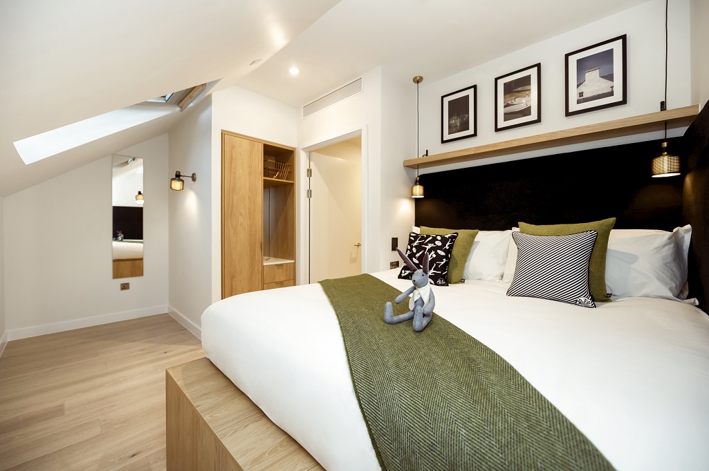 A modern bedroom with a large white bed and green stripe. There is a rabbit teddy sitting on it
